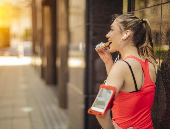 A woman facing away, wearing running attire, and eating a protein bar.