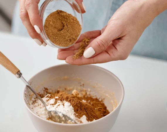 A person pouring a brown powder into a bowl with white flour.