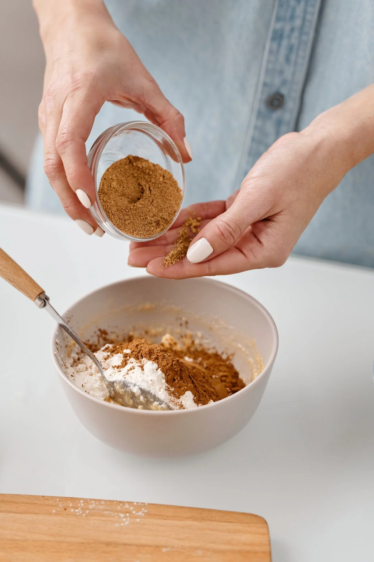 A person pouring a brown powder into a bowl with white flour.