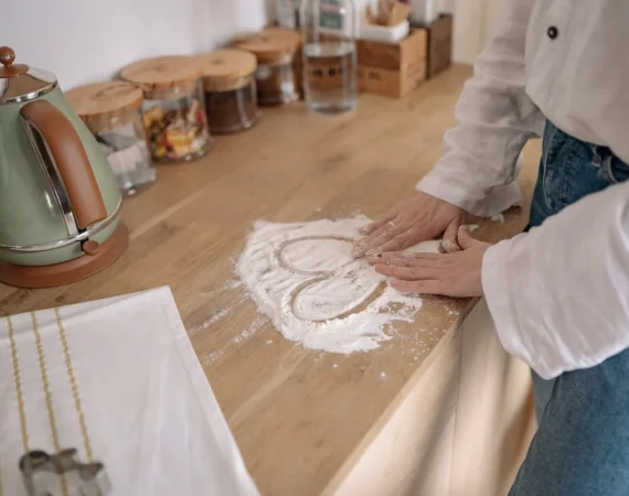 A picture of a kitchen counter with a white powder on it, and the outline of a heart made my someone’s finger in the middle of it, and spices in the background