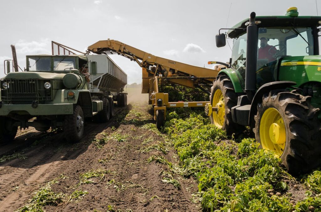 A picture of a tractor and truck in a field, as the tractor pours items into the back of the truck.