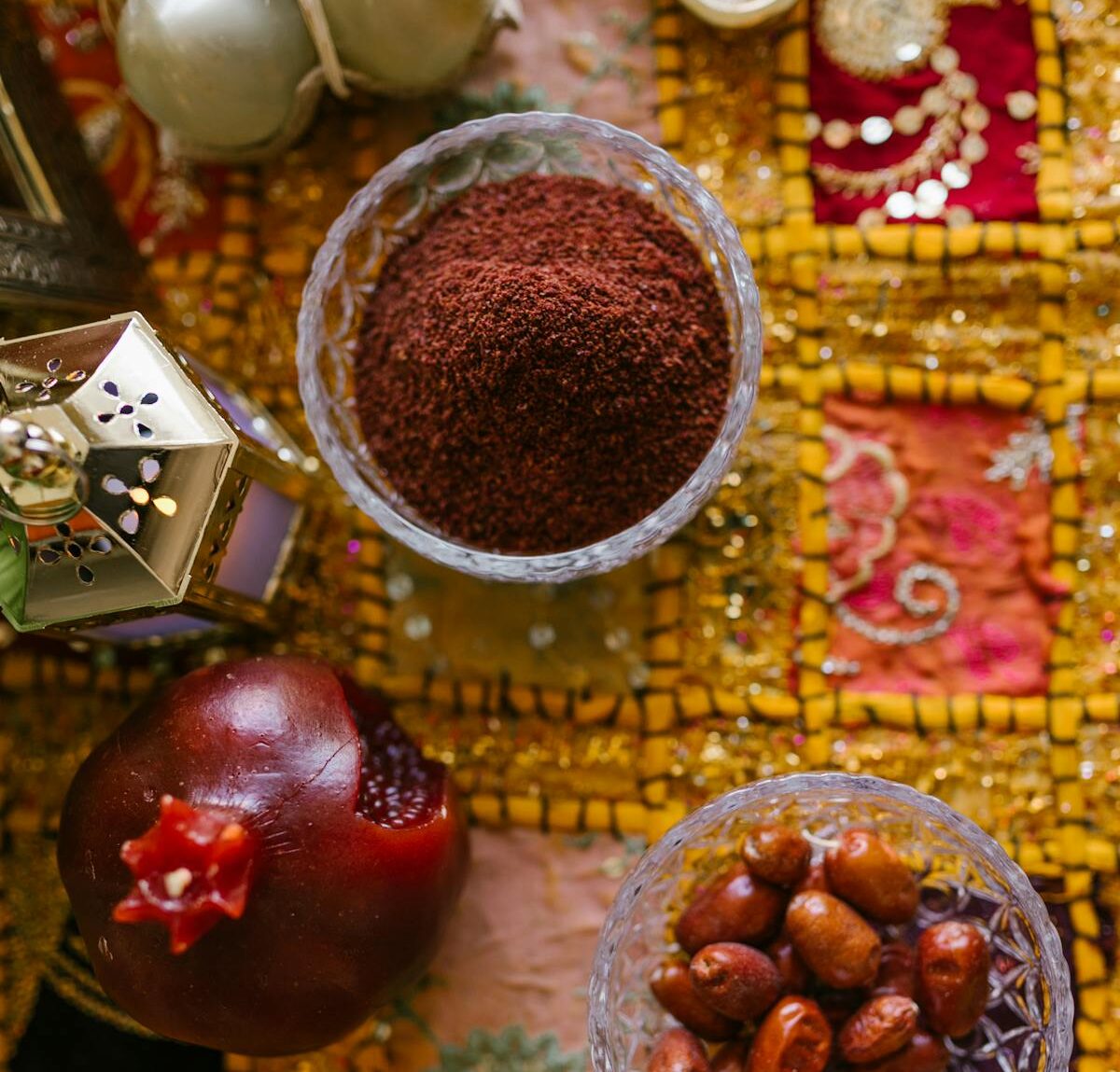 I picture of some food on a table cloth, including a pomegranate, dates, and a brown powder